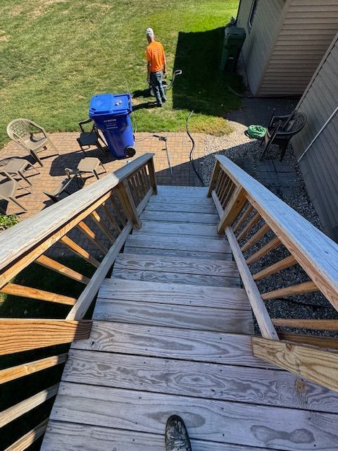 Wooden stairs leading down to a backyard with a person standing near trash bins and grass.