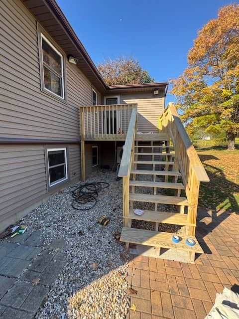 Exterior view of a house with wooden stairs leading to a deck, gravel and a brick patio.