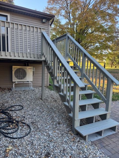 Gray outdoor staircase leading to a deck, set against a gravel ground, and building.