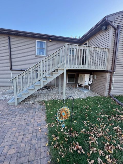 Deck with stairs attached to a beige house, next to a brick patio.