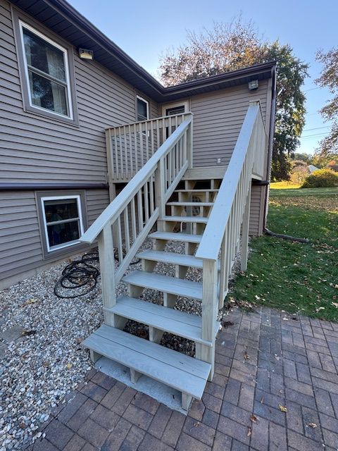 Exterior staircase leading to a wooden deck with gray painted steps and railings, next to a house with gray siding.