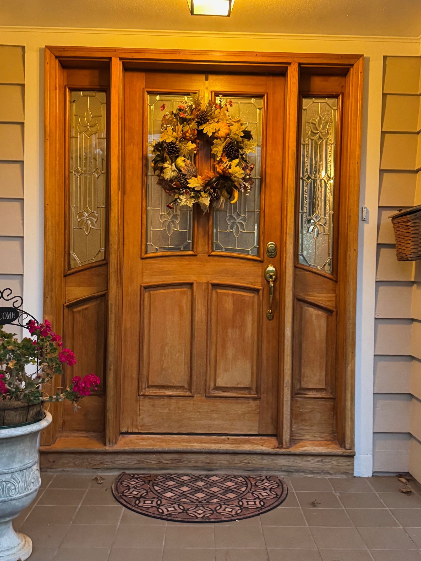 Wooden front door with sidelights, autumn wreath, and welcome mat.