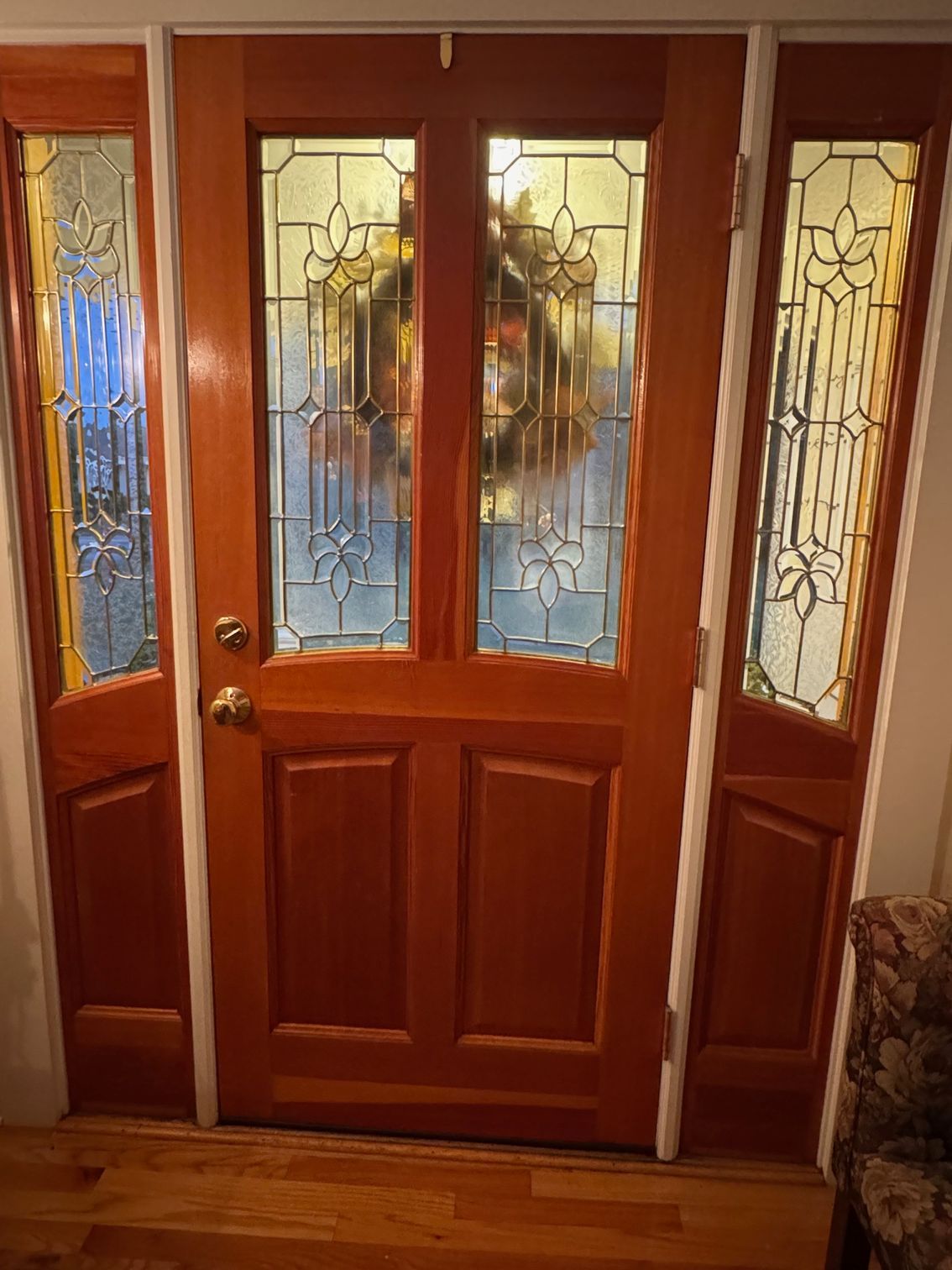 Wooden front door with glass panels and sidelights; a wreath is visible through the door.