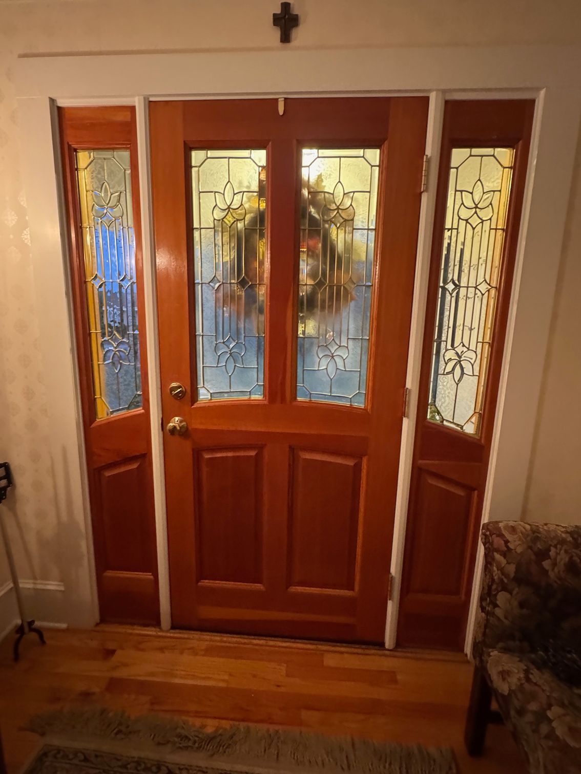 Wooden front door with sidelights, featuring stained glass and a decorative wreath.