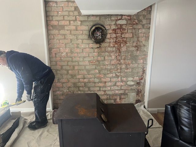 Person installing a wood stove. A brick fireplace is exposed.