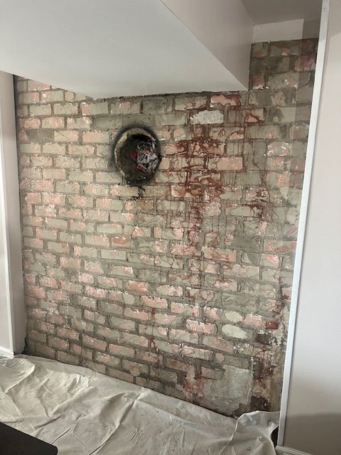 Exposed brick wall with a circular vent, showing red-toned staining and construction debris.