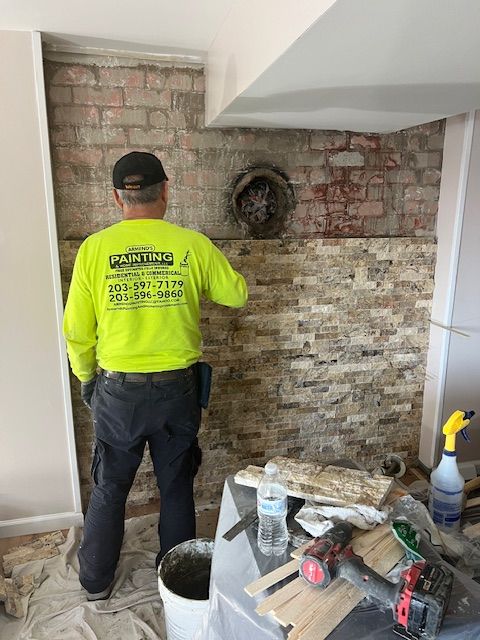 A worker in neon yellow shirt tiling a brick wall. Construction tools and supplies are nearby.