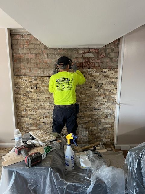 A worker in a neon yellow shirt installs stone tiles on a wall indoors.