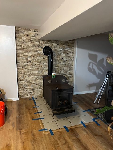 Wood-burning stove installed in a room with brick-style accent wall and tiled hearth, on wood-look flooring.