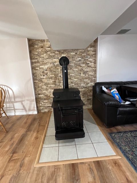Black wood-burning stove on tiled hearth, against a stone-look wall in a room with wood flooring.