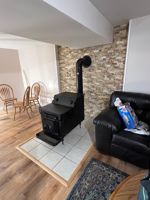 Black stove with chimney, on tiled hearth, next to brick wall and leather couch.