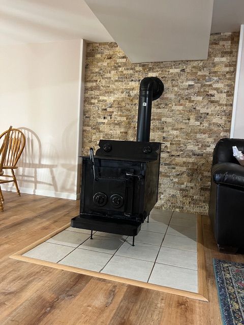 Black wood-burning stove on tiled hearth, against a brick wall, inside a room with wood flooring.