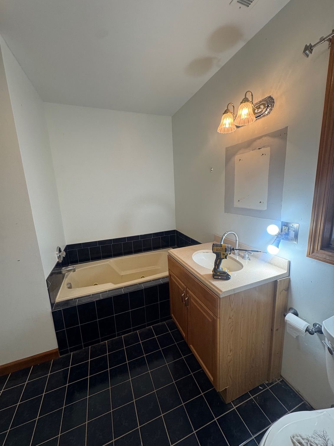 Bathroom with a jacuzzi tub and a vanity. Black tiled floor and walls. Natural light from the window.
