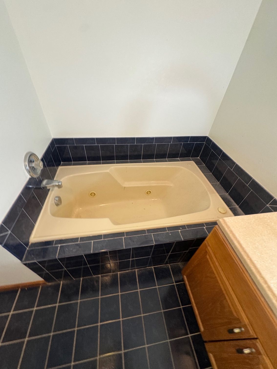 Built-in beige bathtub with dark blue tile surround in a corner of a bathroom.