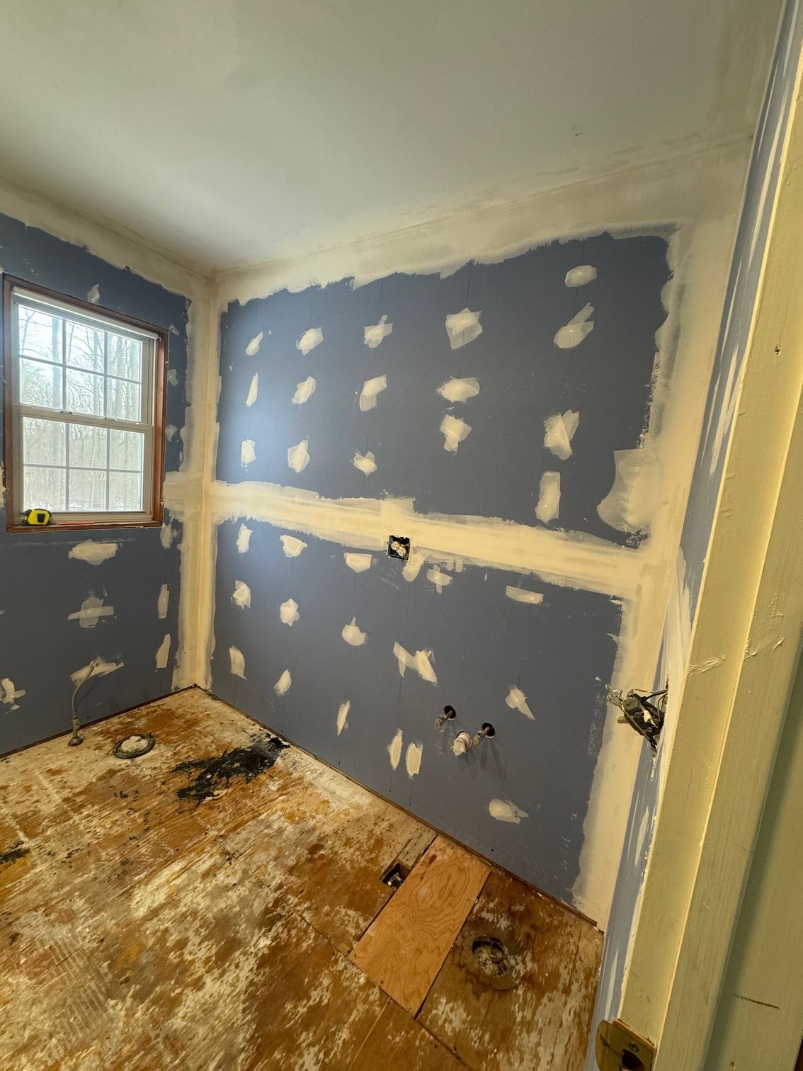 Room under construction with blue drywall, white spackling, and wooden floor.