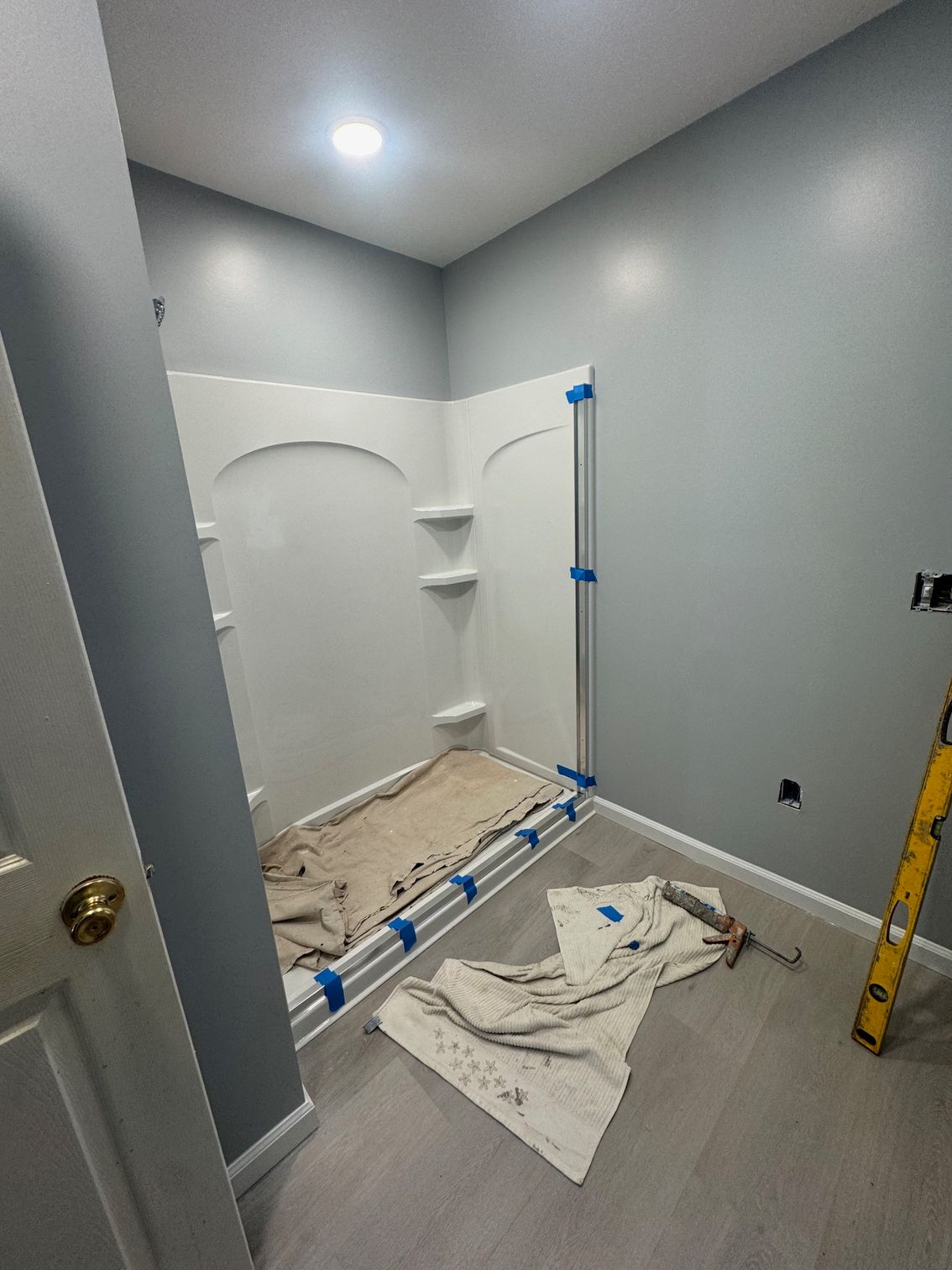 Bathroom with white shower stall, light gray walls, gray flooring, and painter's tape; still under construction.