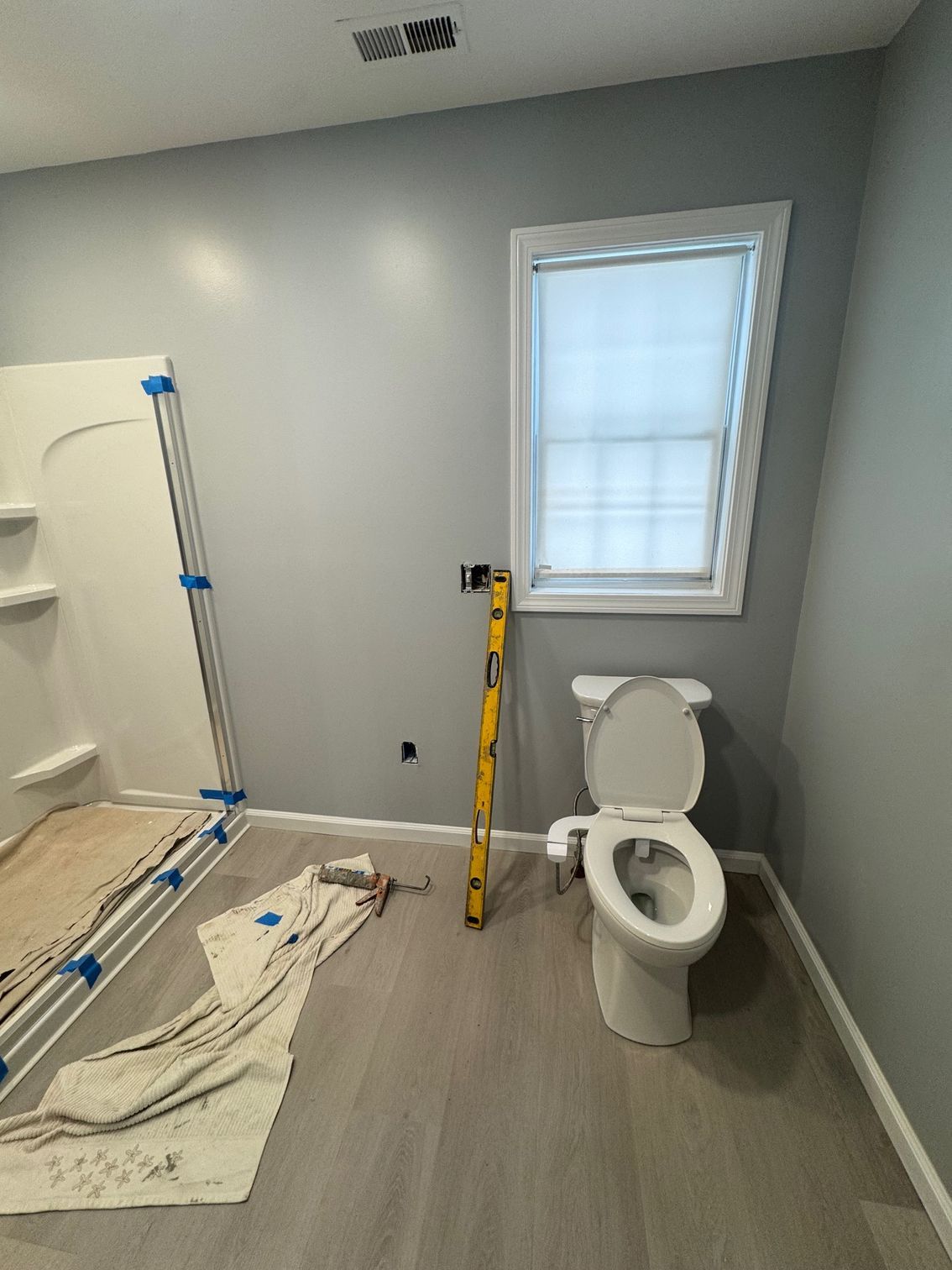 Bathroom under construction: gray walls, light floor, toilet, window, level, and a shower stall.