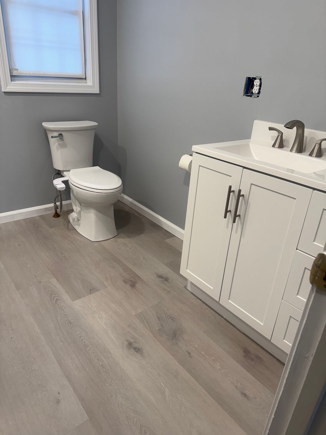 Bathroom with a toilet, white vanity, and light gray flooring. Gray walls and a window are visible.