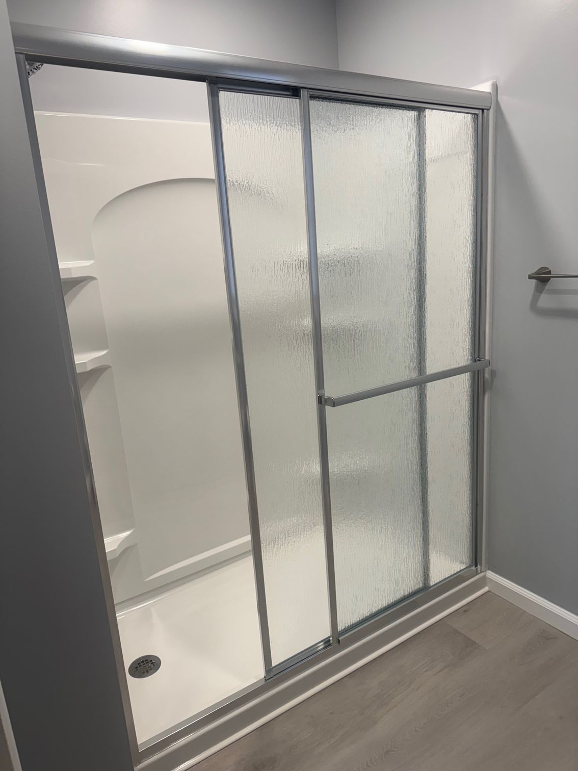 Shower stall with sliding glass doors, textured glass, and a white interior.
