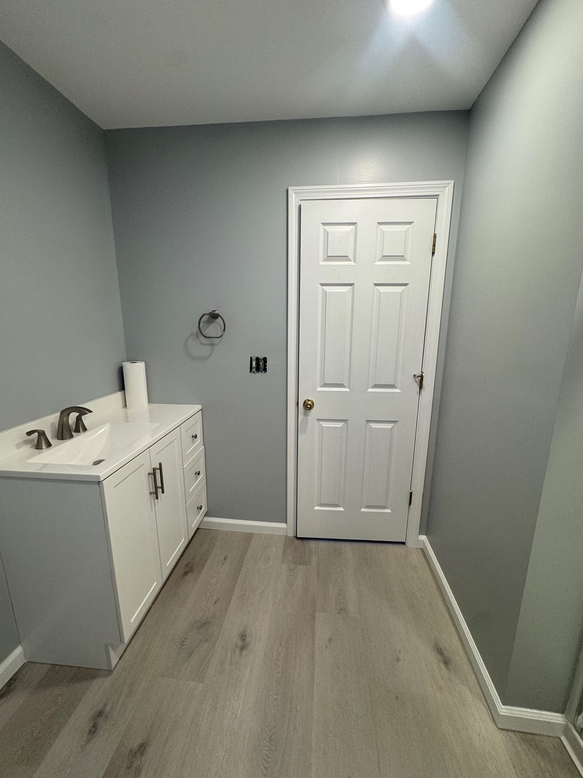 Bathroom with white vanity and door, gray walls, and light wood-look flooring.
