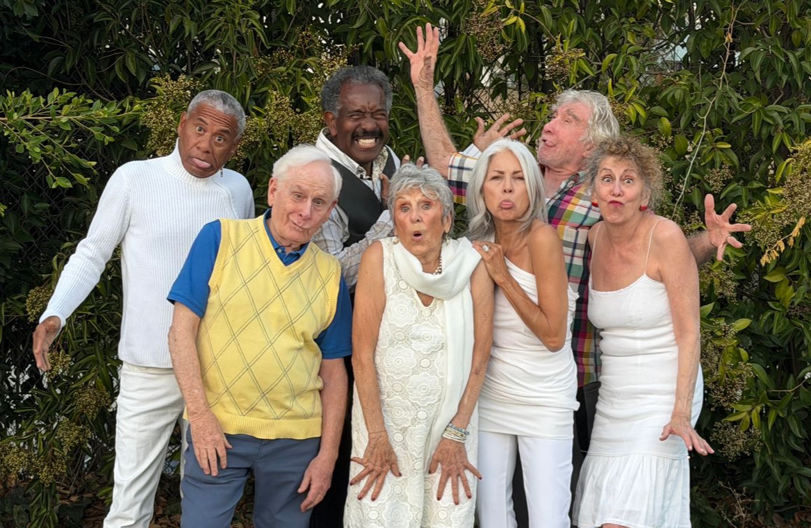 Group of people making surprised, expressive faces, posing outside by greenery.