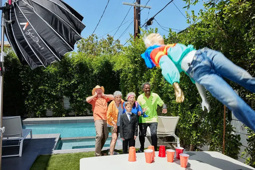 Group of people reacting to a doll flying through the air near a pool.