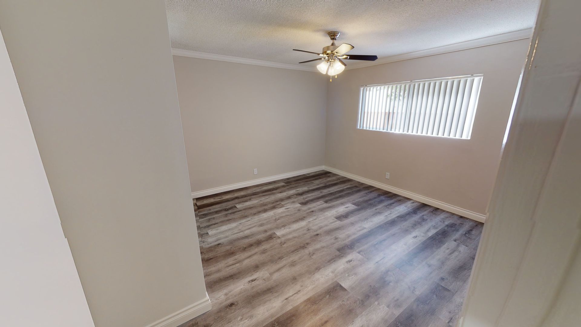 Empty bedroom with wood-look flooring, tan walls, ceiling fan, and window with blinds.