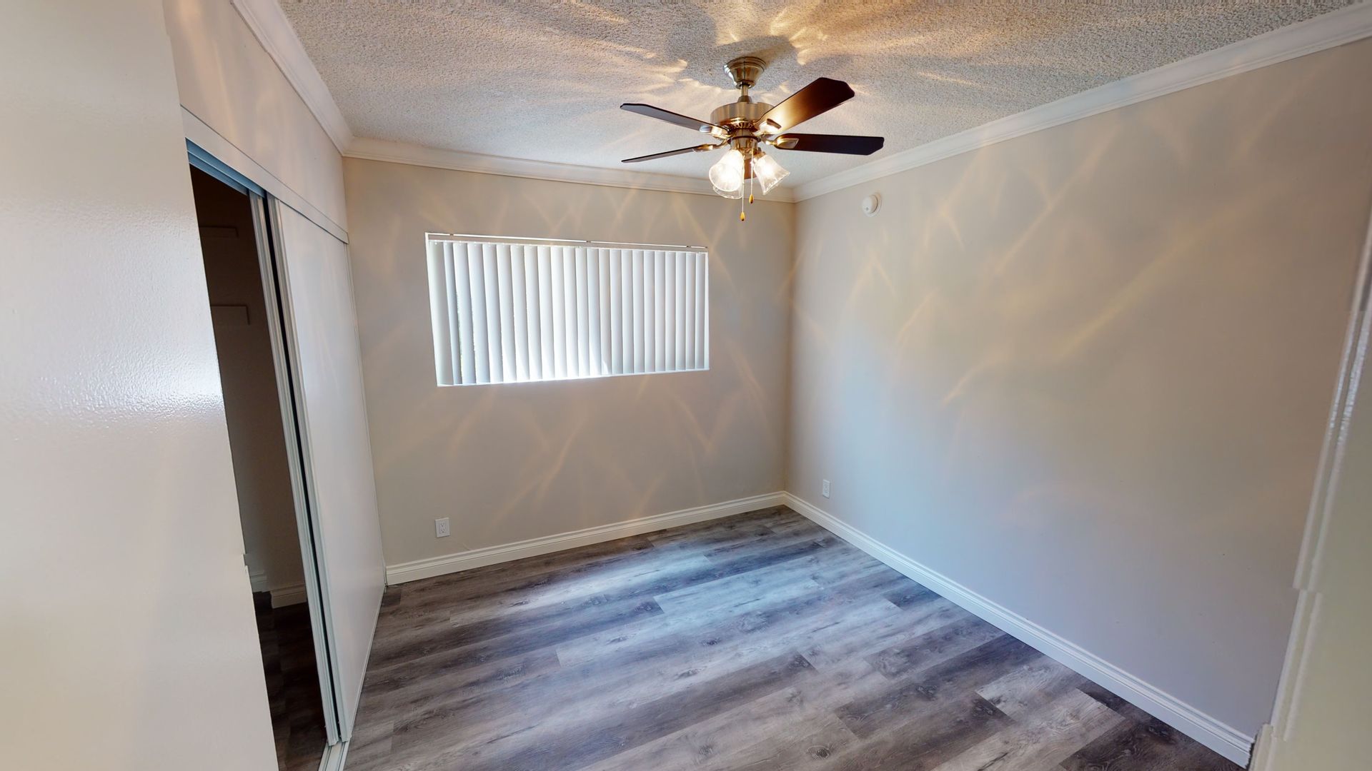 Empty room with a ceiling fan, window with blinds, and wood-look flooring.