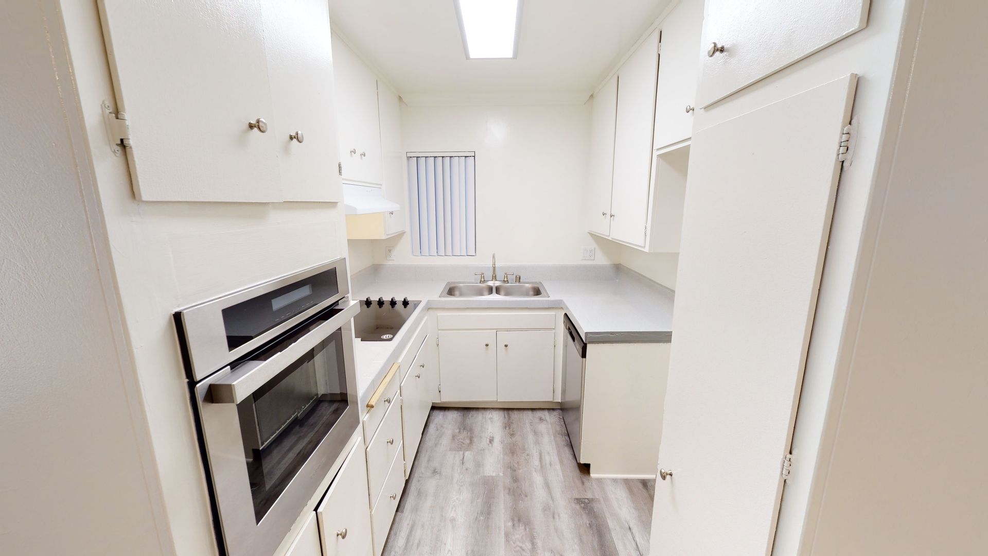 Narrow, bright kitchen with white cabinets, stainless steel oven, and light gray countertops.