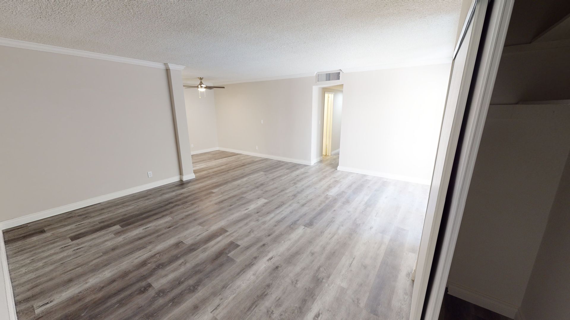 Empty room with gray wood-look flooring, white walls, and a doorway leading to another room.