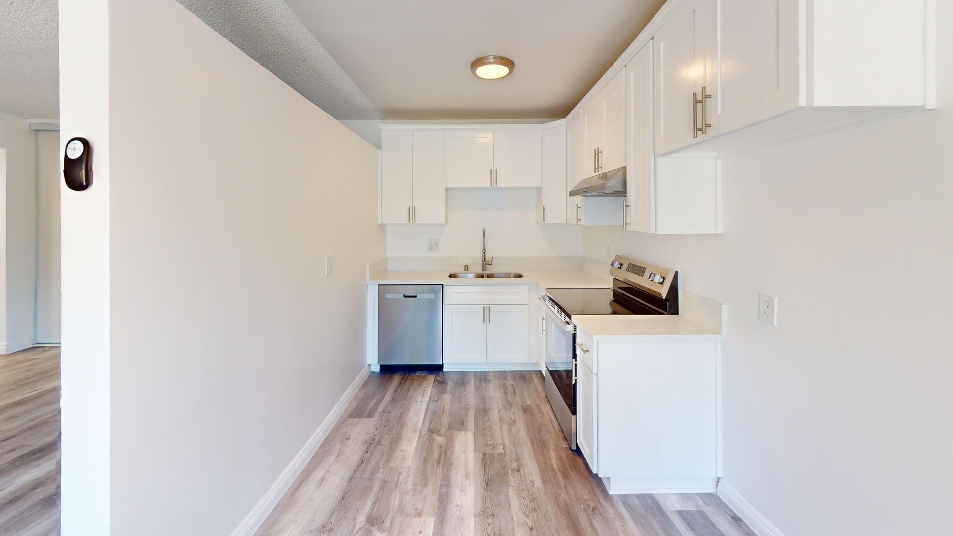 A white kitchen with wooden floors. Includes stainless steel appliances, white cabinets, and a sink.