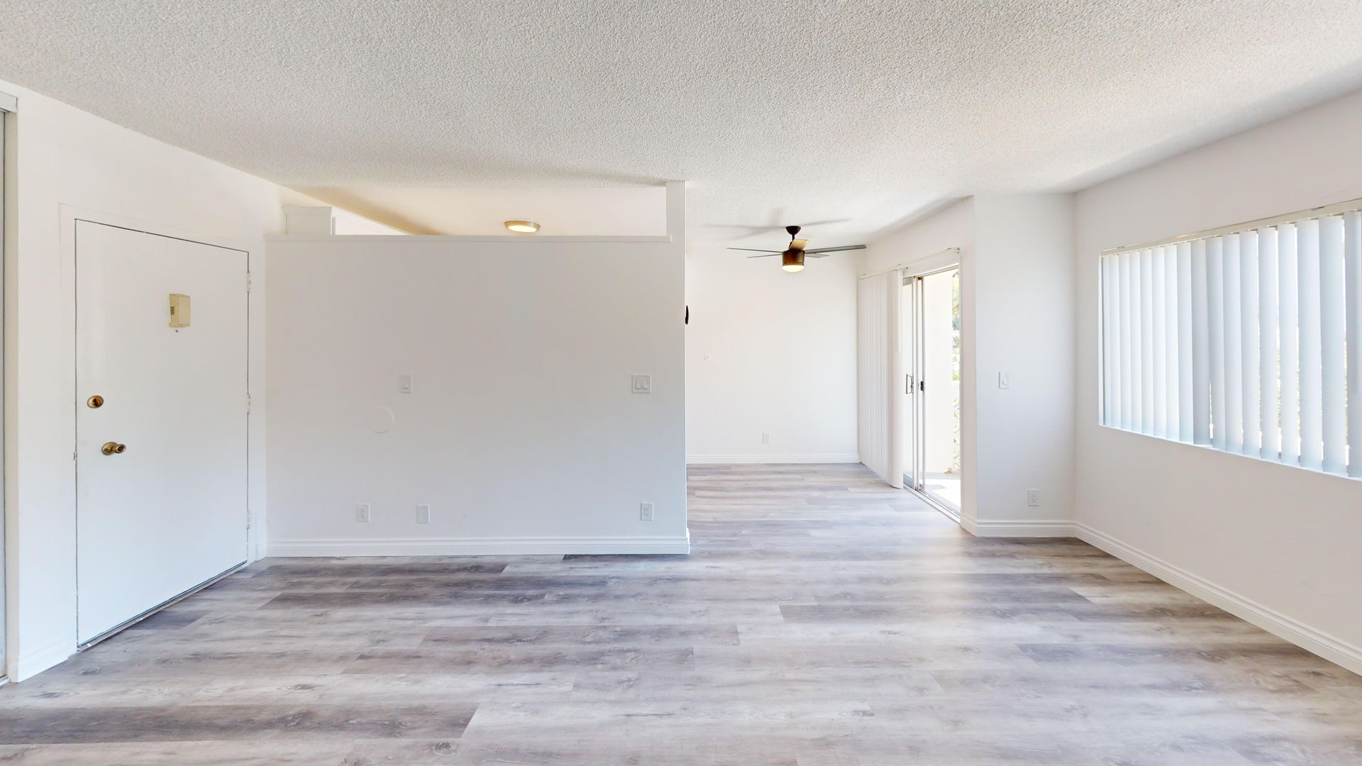 Interior view of an apartment with white walls, gray wood-look flooring, and a sliding glass door.