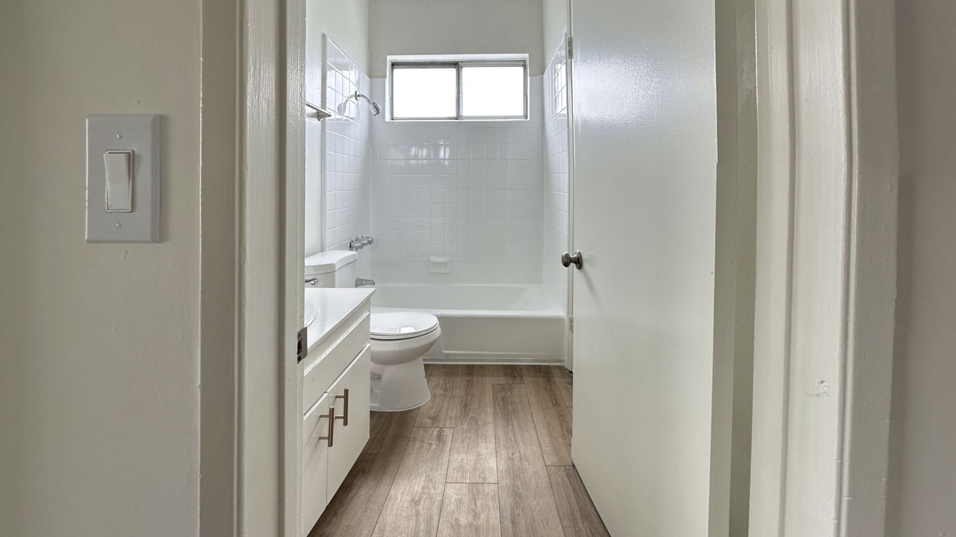 Bathroom interior with white walls, a bathtub, and a wooden floor.