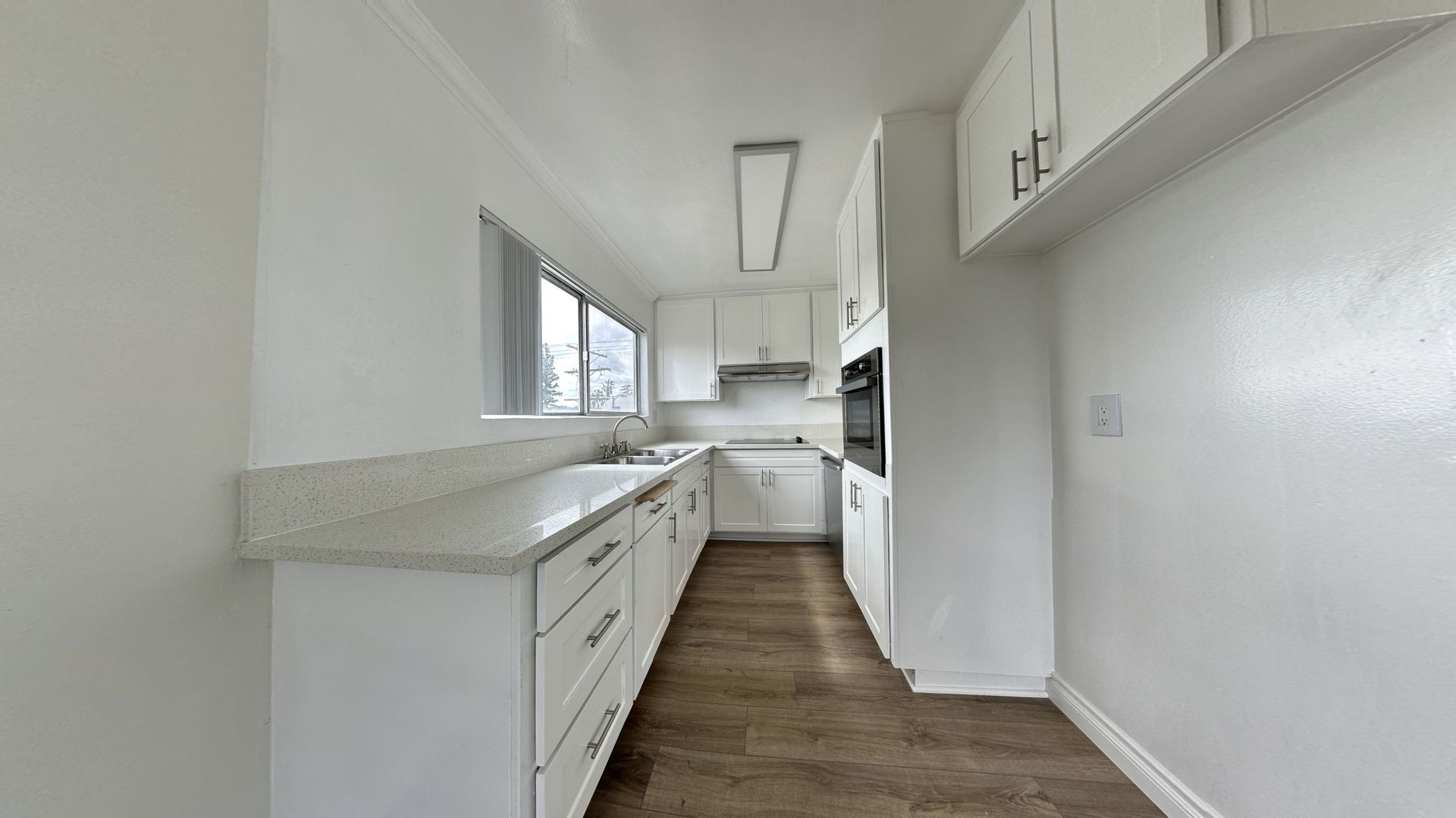 White kitchen with white cabinets, countertops, and appliances. A window and oven are visible.