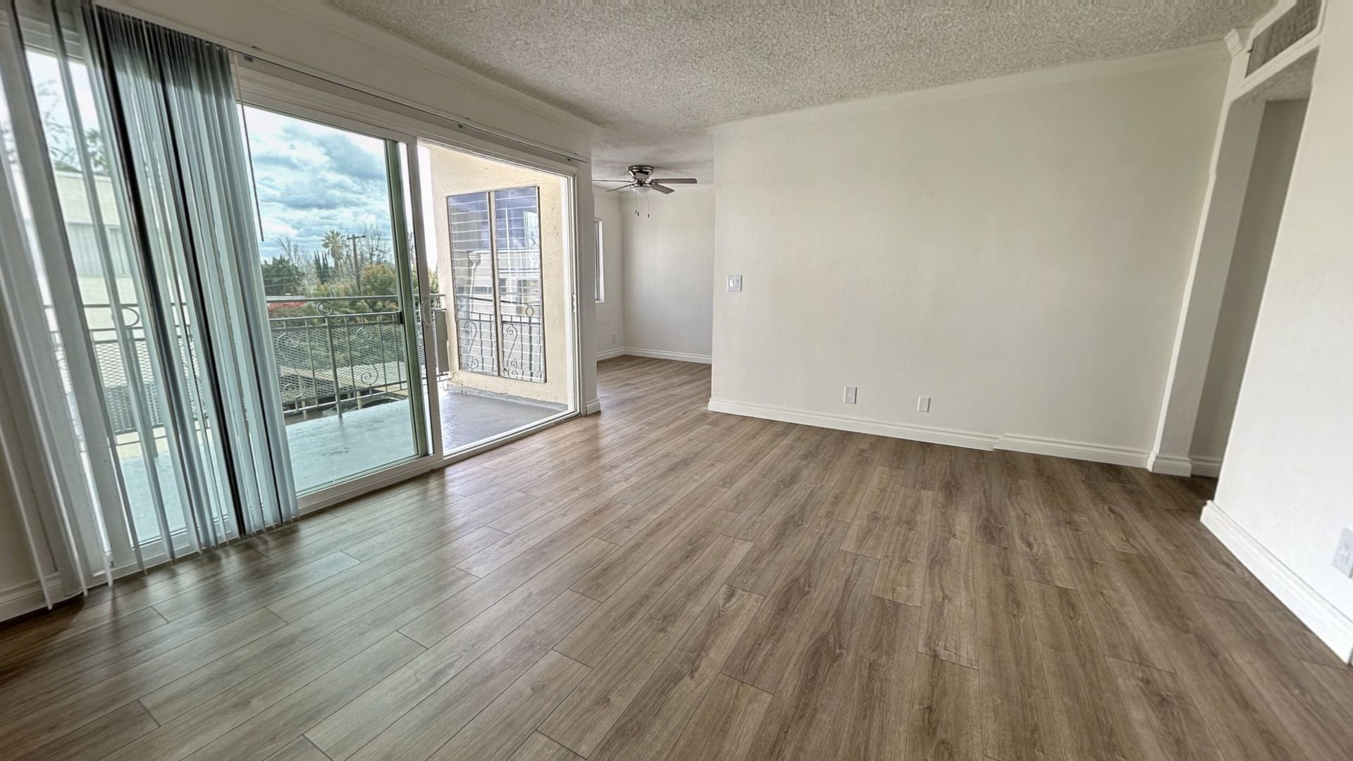 Empty living room with wooden floors, large sliding glass door, and white walls.