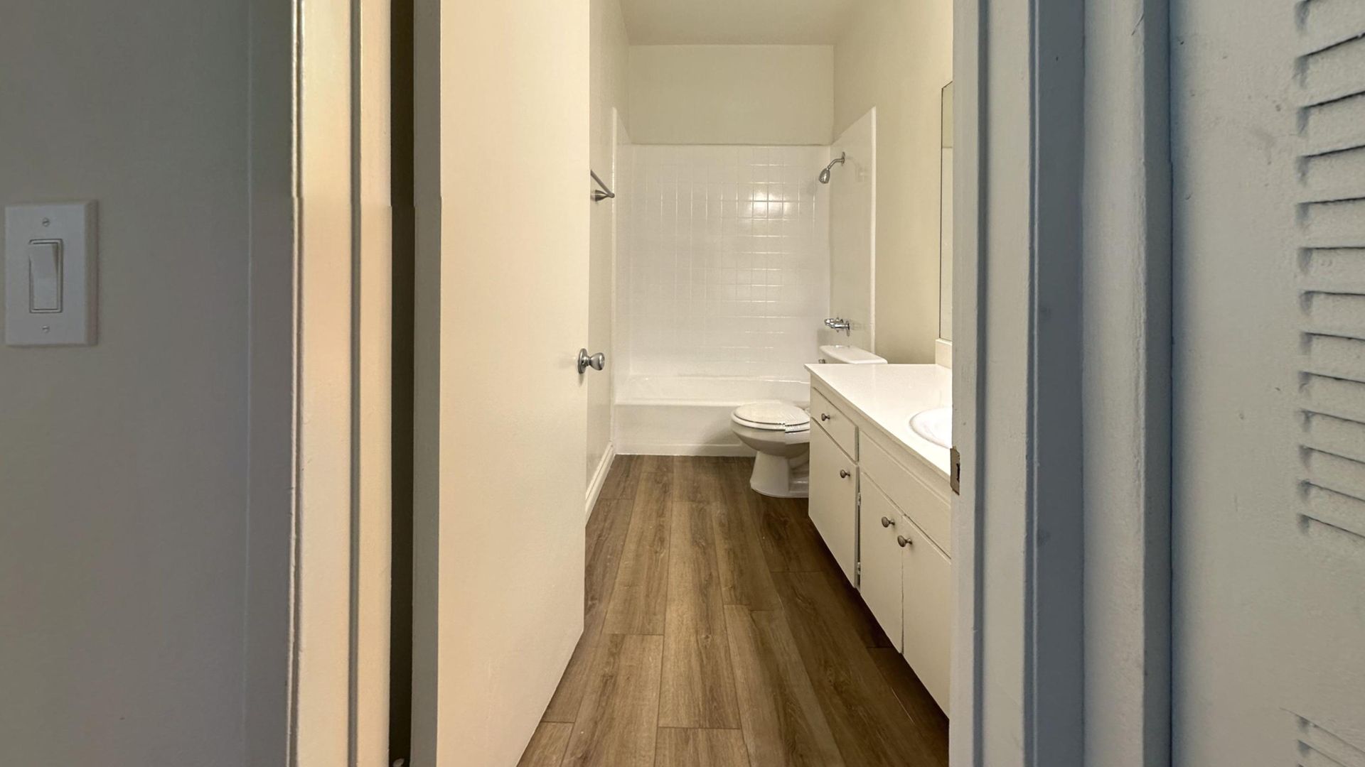 Bathroom with white walls, cabinets, and a bathtub; wooden-look floor.
