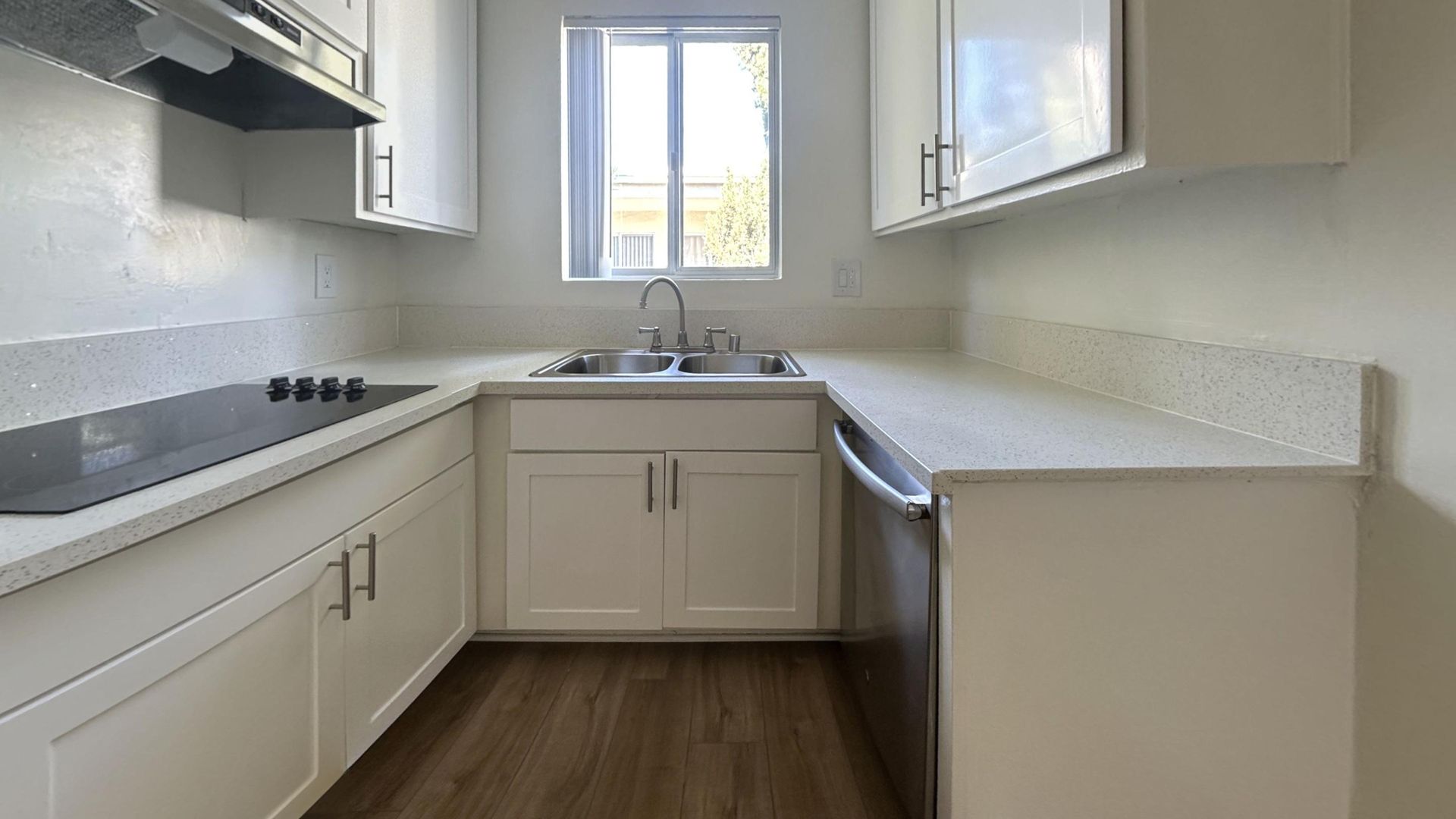 A small, white kitchen with a window above the sink and stainless steel appliances.
