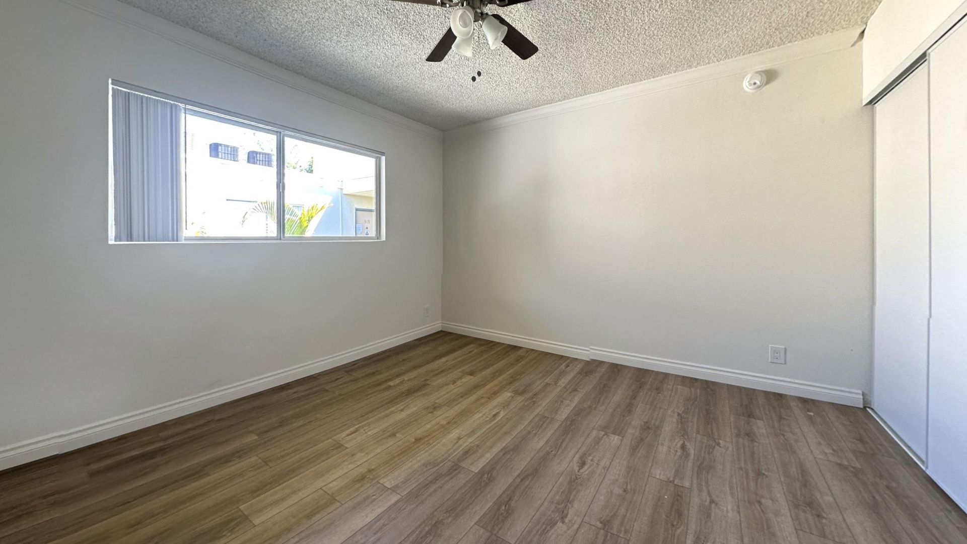 Empty room with wood-look floor, window, ceiling fan, and white walls and closet.