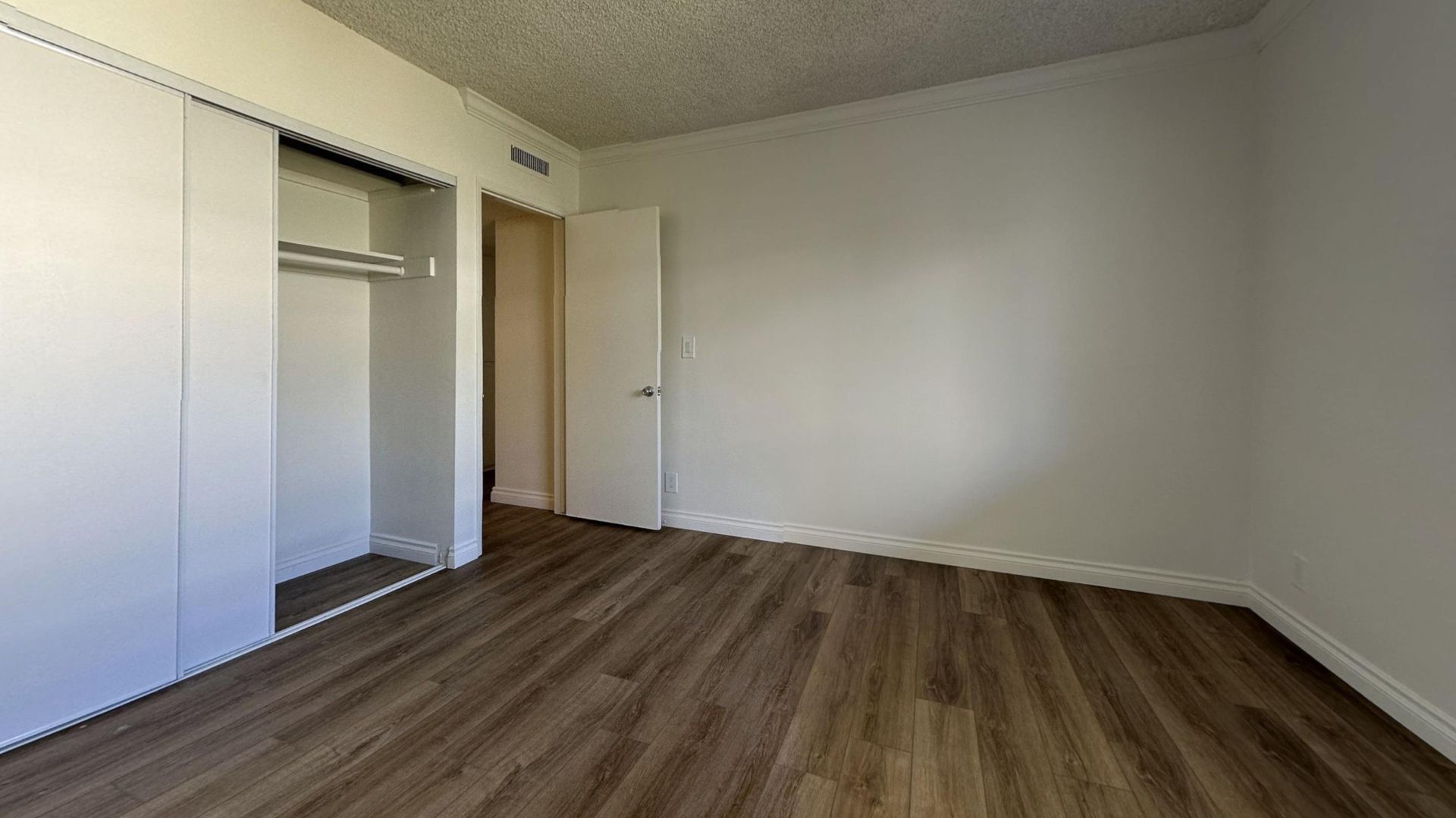 Empty bedroom with wood-look flooring, white walls, closet, and a doorway.
