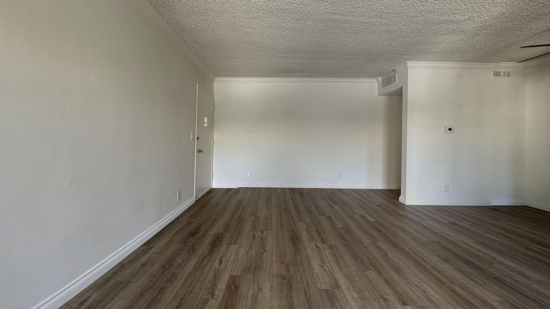 Empty living room with light wooden floors, white walls, and popcorn ceiling.