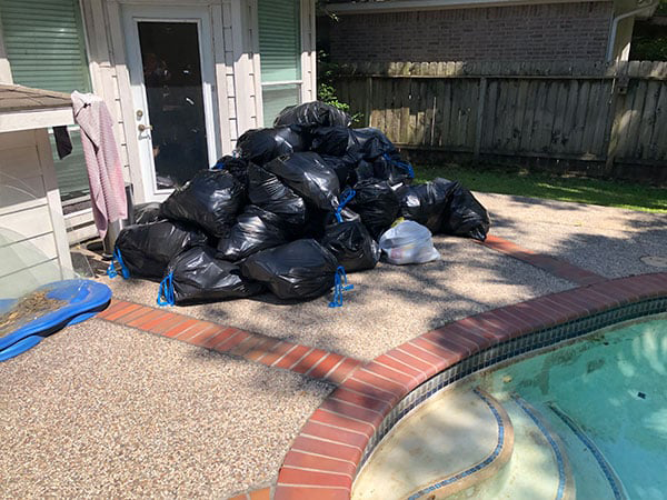 pile of black garbage bags full of house junk outside house