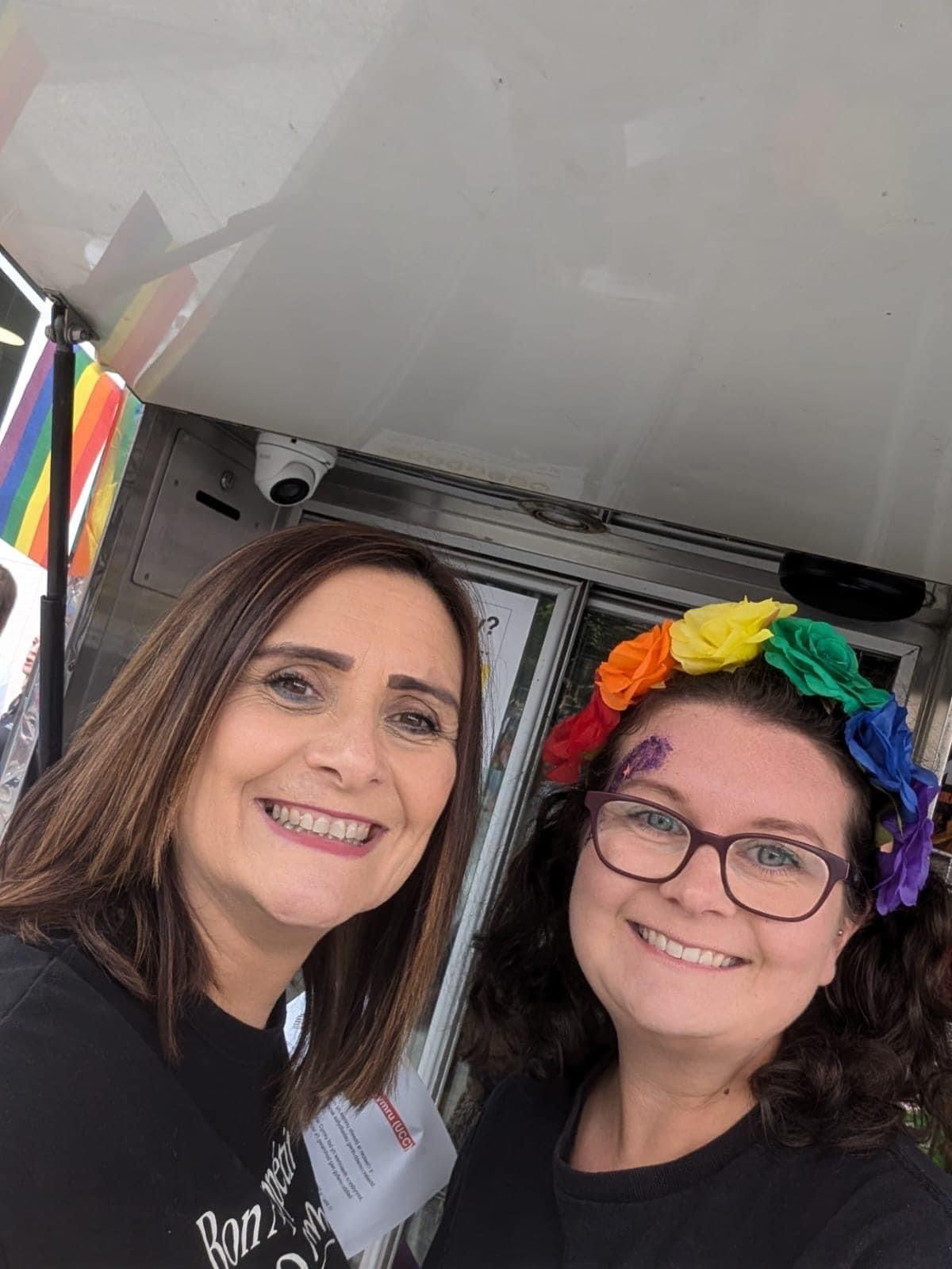 Two women are posing for a picture and one of them is wearing a rainbow headband.