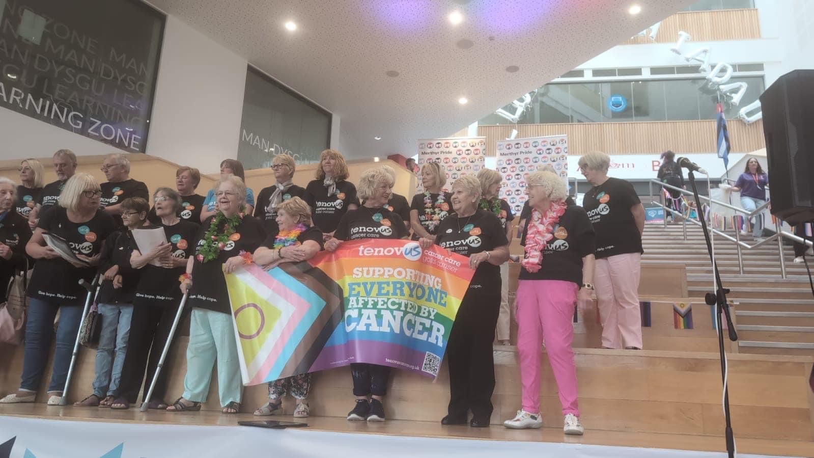 A group of people are standing on a stage holding a rainbow flag.