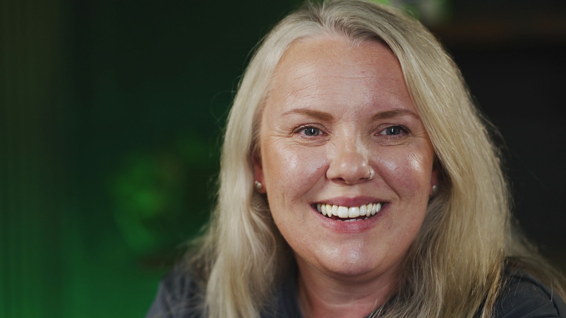 A close up of a woman smiling in front of a green background.