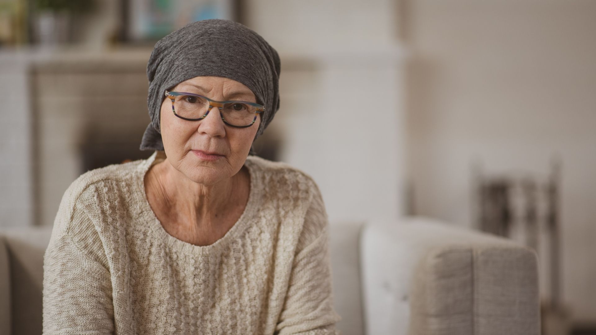 A woman with cancer is wearing a head scarf and glasses.