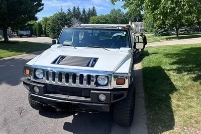 White Hummer SUV parked on a grassy curb beside a sidewalk in a sunny suburban park area