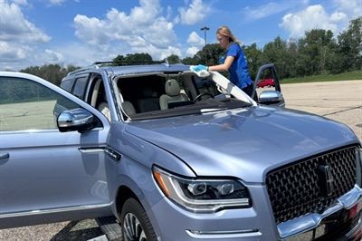 Woman leaning into a silver SUV with open door in a parking lot under a blue sky