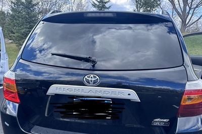 Rear view of a dark blue Toyota Sienna parked outdoors, with a rear windshield wiper and cloudy sky reflection.