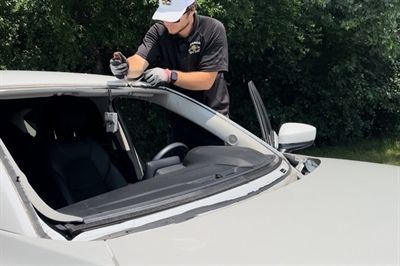 Person cleaning the roof of a white car with a spray bottle outdoors