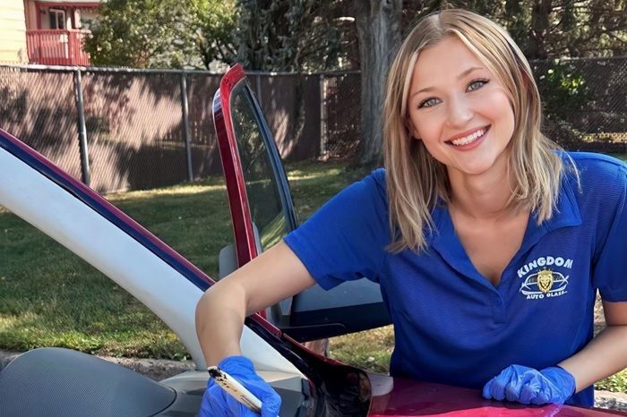 Smiling woman in blue shirt leaning into an open car door, holding a tool and pink cloth outdoors